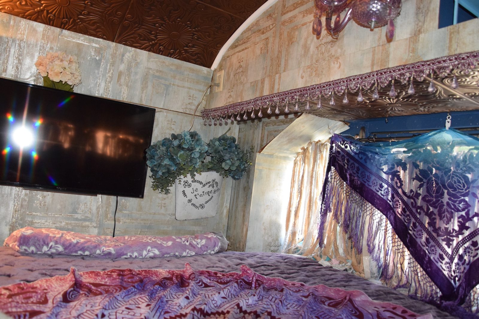 Bedroom wall with a 'Je t'aime' flower planter, beaded valance, and a purple velvet shawl draped over the window