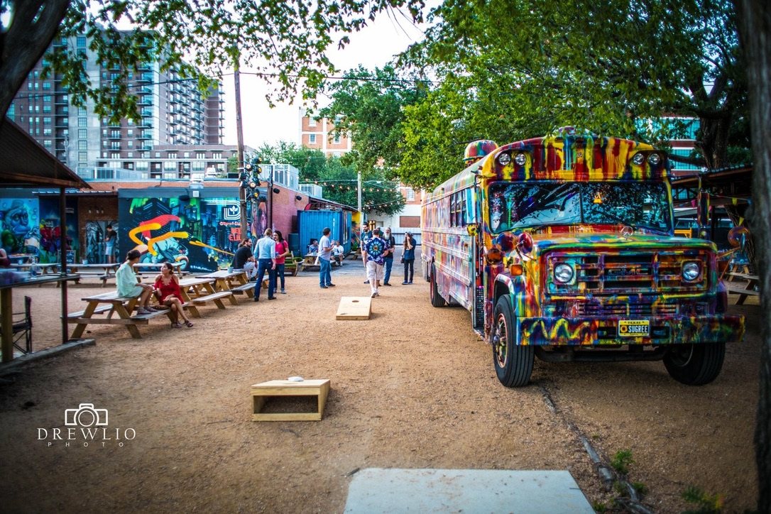 SUGAREE parked at an outdoor beer garden at dusk, people at picnic tables and a cornhole game in the foreground