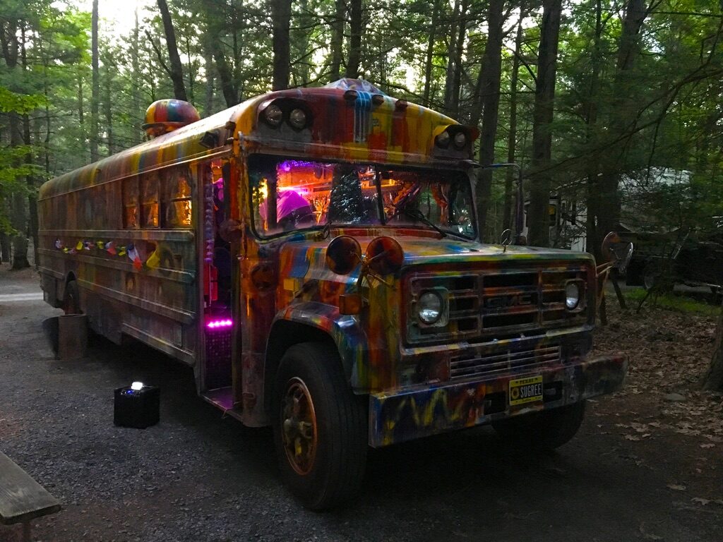 SUGAREE parked at a wooded campsite at dusk, interior lights glowing purple