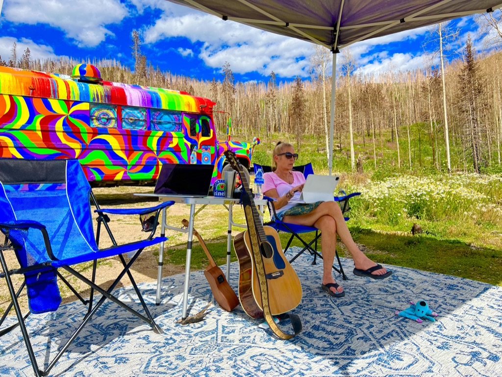 Kelly sitting under the canopy with a laptop and two guitars leaning nearby