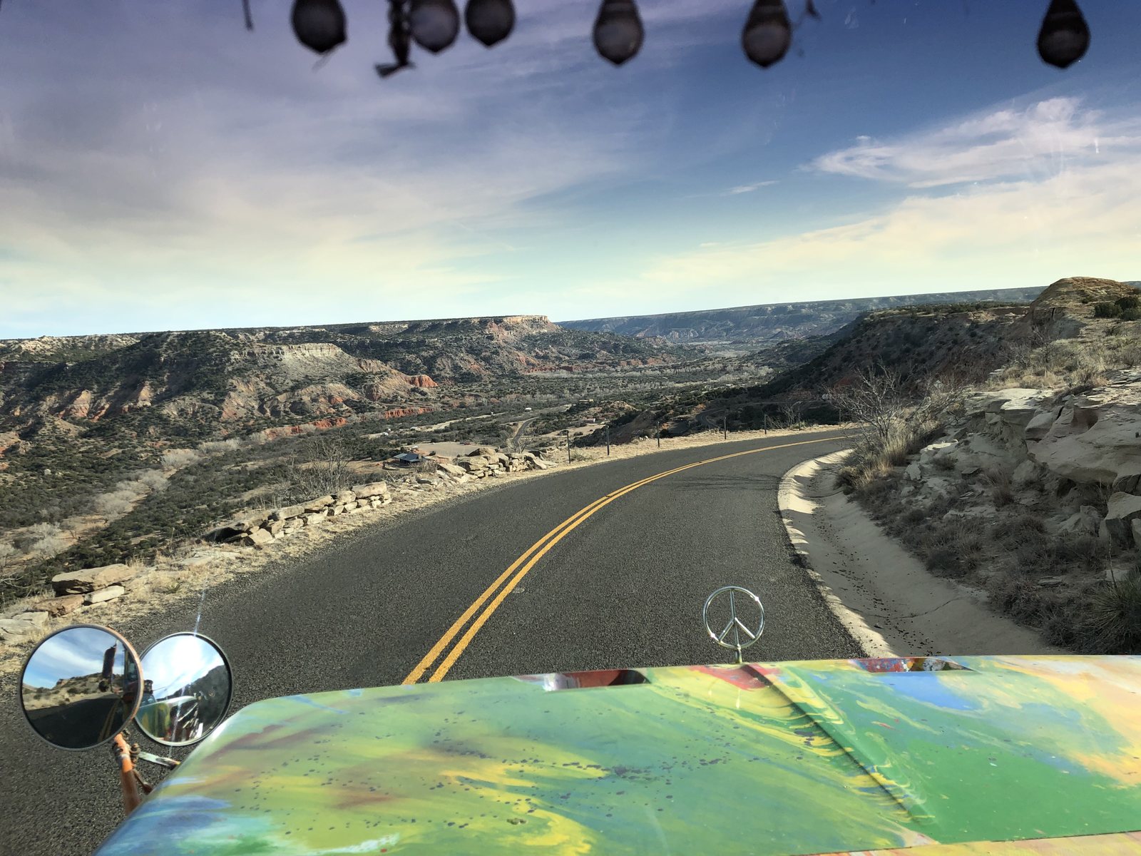 Windshield view of the road dropping down into a wide desert canyon