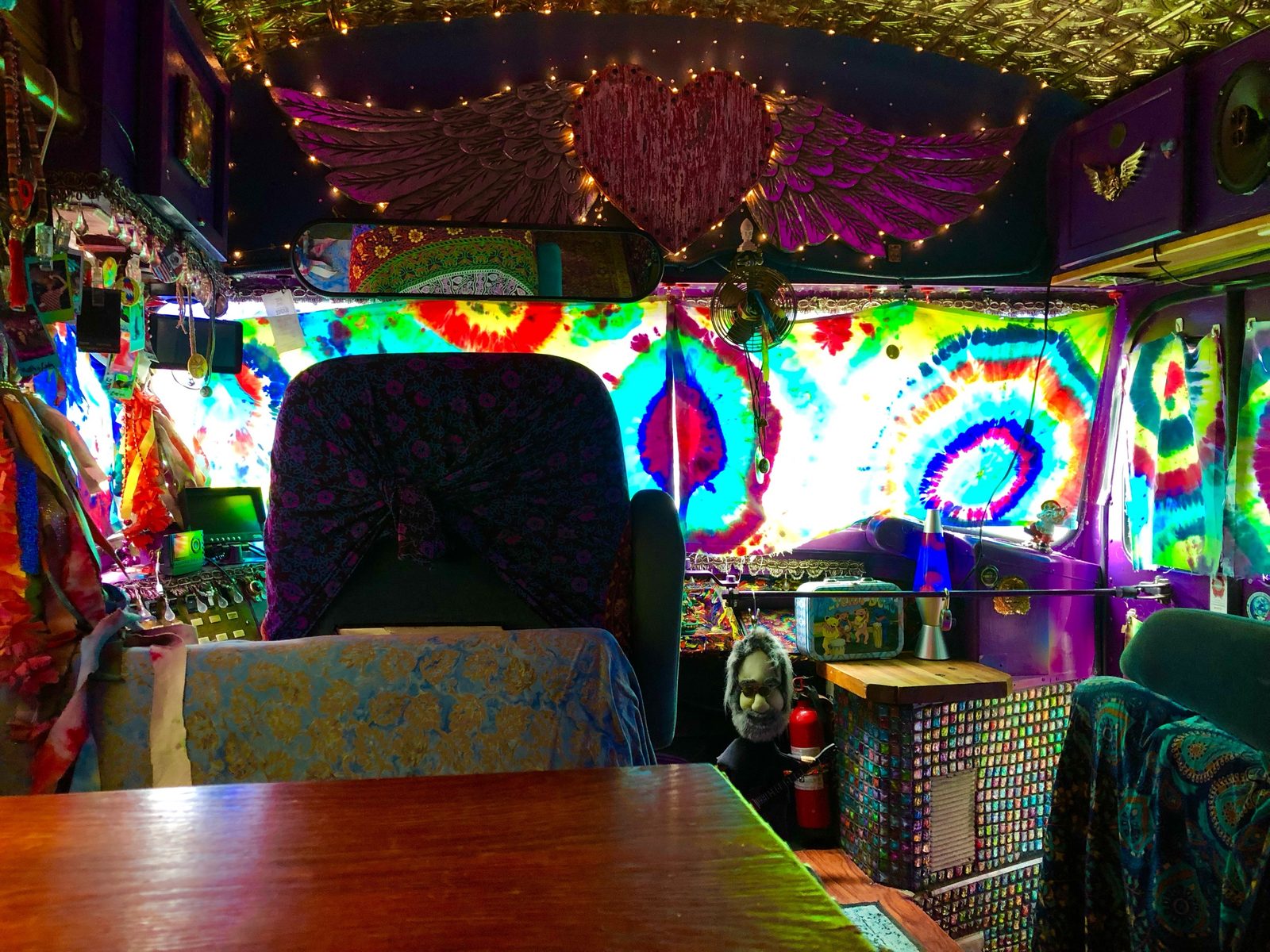 SUGAREE's cockpit with backlit tie-dye curtains, a carved winged heart above the windshield, and string lights on the tin ceiling