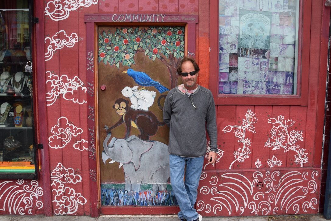 A man standing beside a hand-painted 'Community' mural door in the Haight