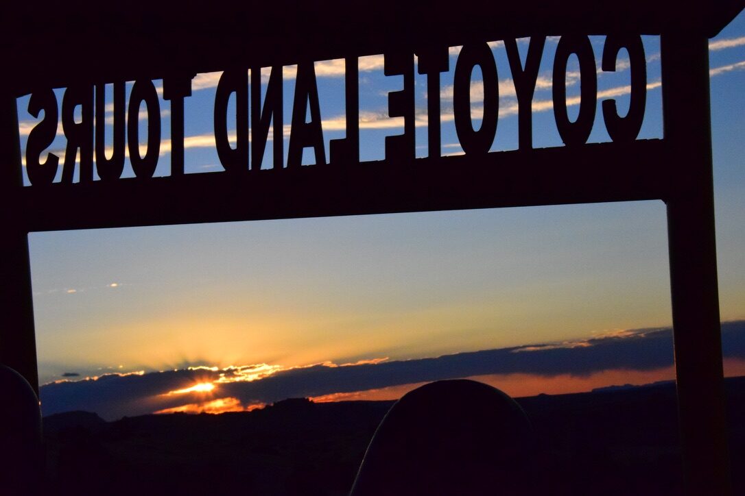 Silhouette of a Coyote Land Tours sign against a desert sunset