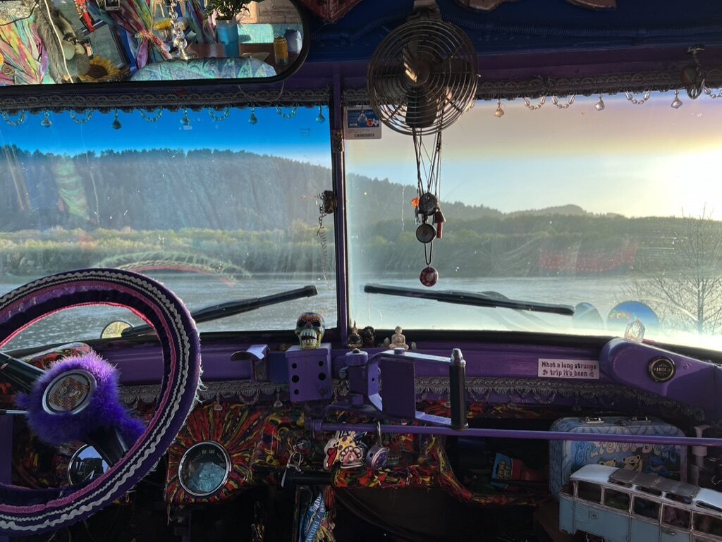 View through SUGAREE's decorated dashboard and windshield, overlooking a river at dawn