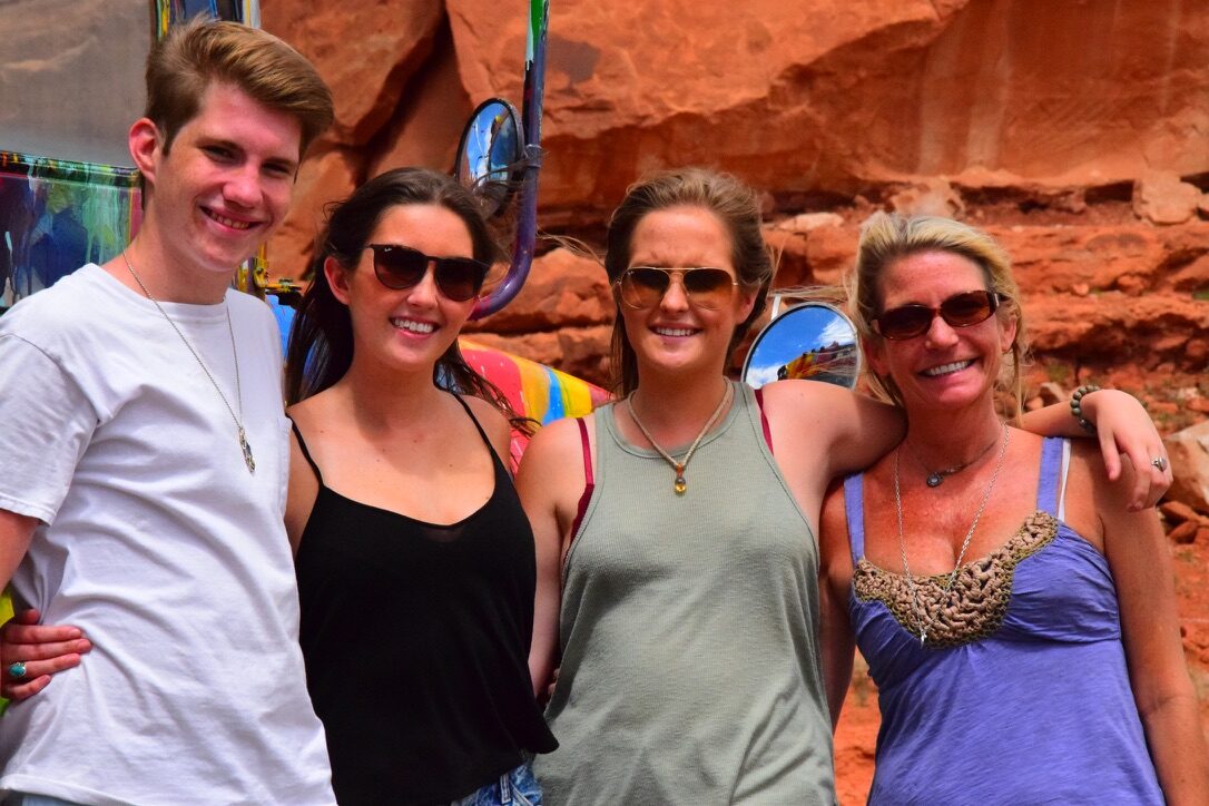 Four friends standing together in front of SUGAREE against a red rock canyon wall