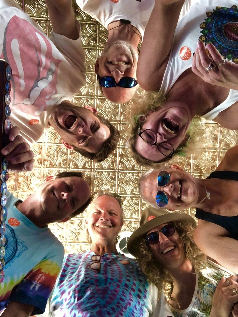 Seven friends in a circle looking down at the camera, laughing, beneath SUGAREE's gold tin ceiling