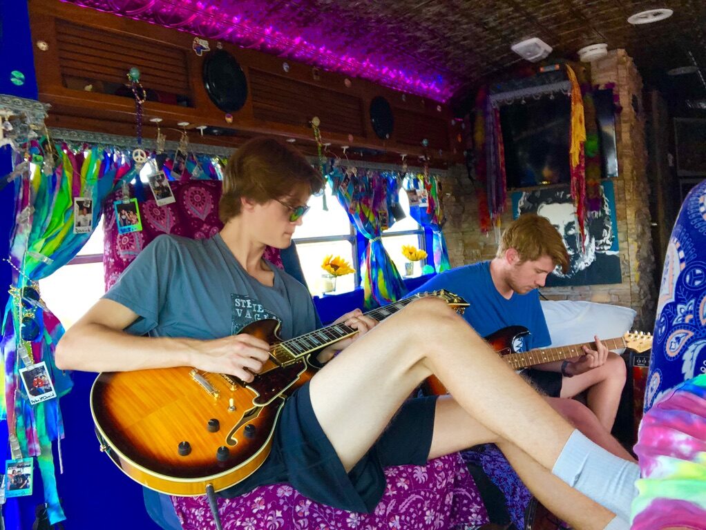 Two friends playing guitar inside SUGAREE, sunflowers on the windowsill