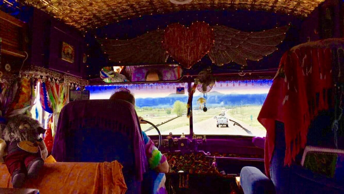 View through SUGAREE's windshield beneath the heart-and-wings decoration, driving through mountain country