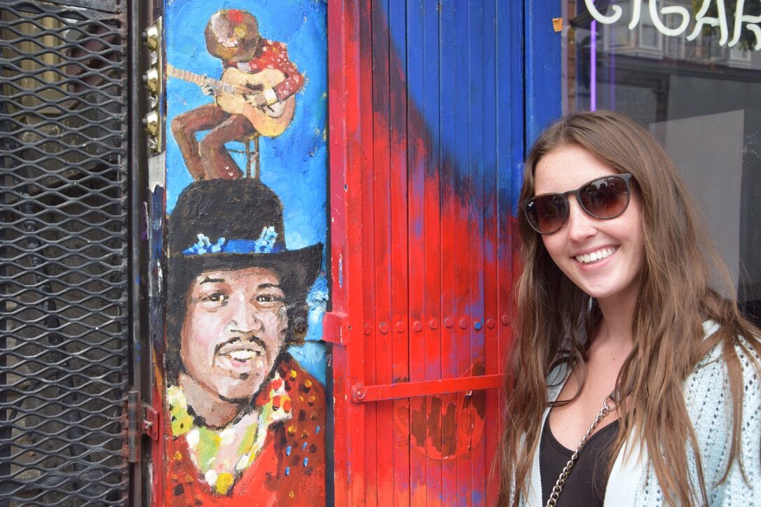 A woman standing beside a painted mural of Jimi Hendrix in the Haight-Ashbury district
