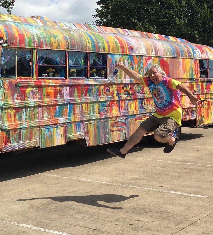 A joyful leap in front of SUGAREE, tie-dye shirt and paint can in hand