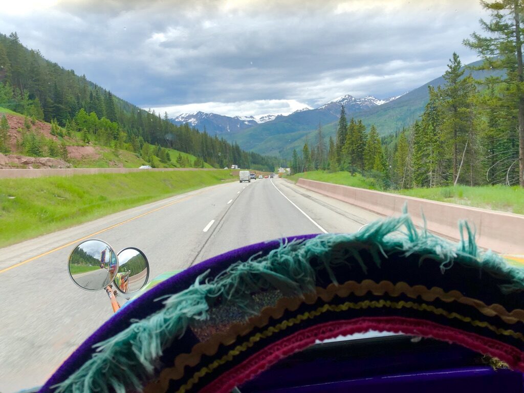 View through SUGAREE's windshield along another mountain highway, snow-capped peaks ahead