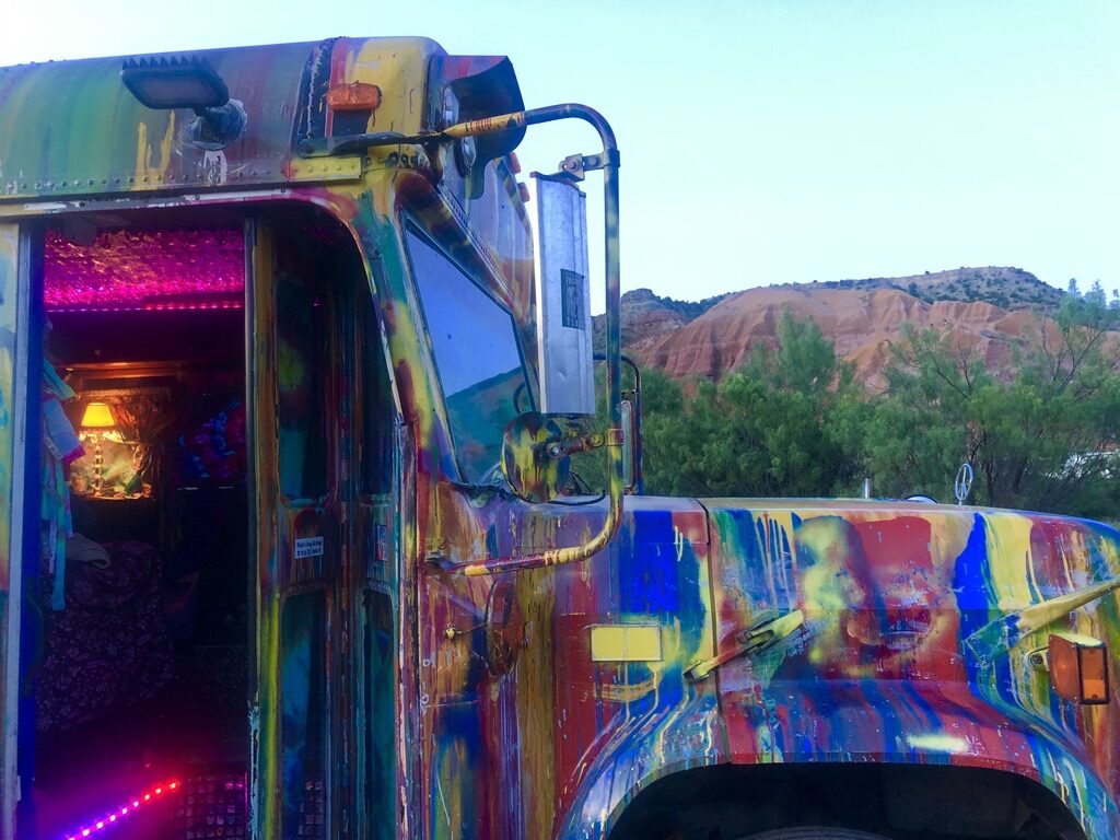 SUGAREE's open side door glowing purple and pink at dusk, red rock hills in the background