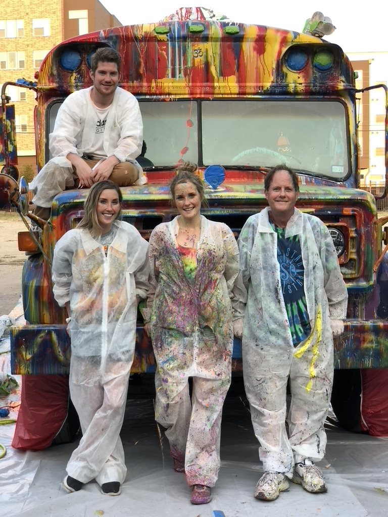 Four painters in paint-spattered coveralls in front of the freshly painted bus