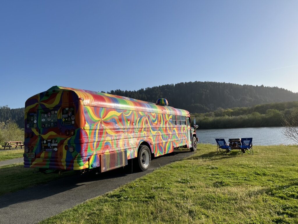 SUGAREE parked on the grass beside a river, camp chairs and table set up nearby