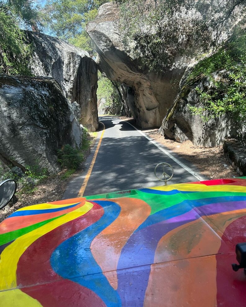 View over SUGAREE's painted hood through a narrow tunnel carved into boulders on a mountain road