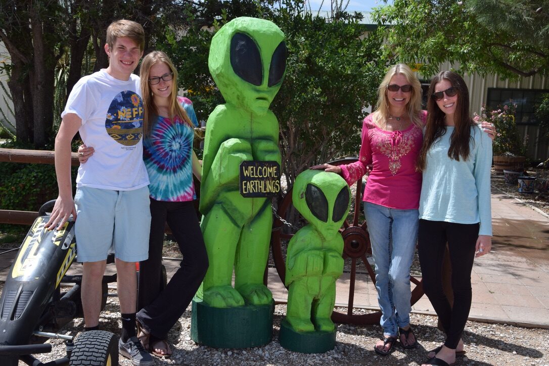 The family posing with alien statues in Roswell, New Mexico, one holding a 'Welcome Earthlings' sign