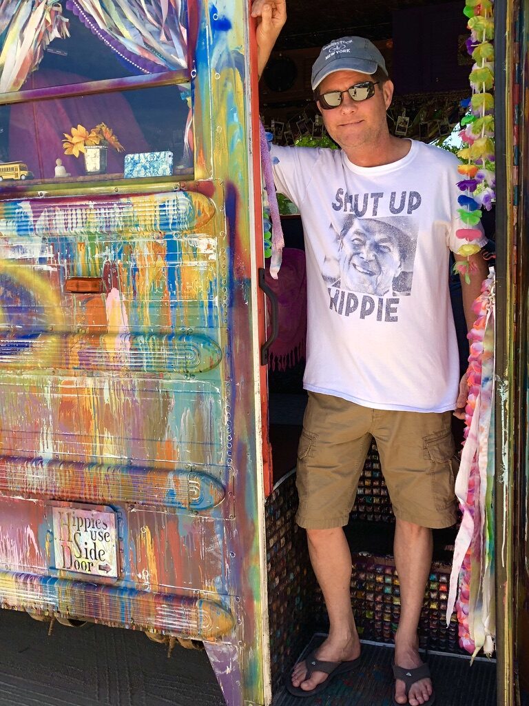 A man in a Shut Up Hippie t-shirt standing at SUGAREE's side door, next to the Hippies Use Side Door sign