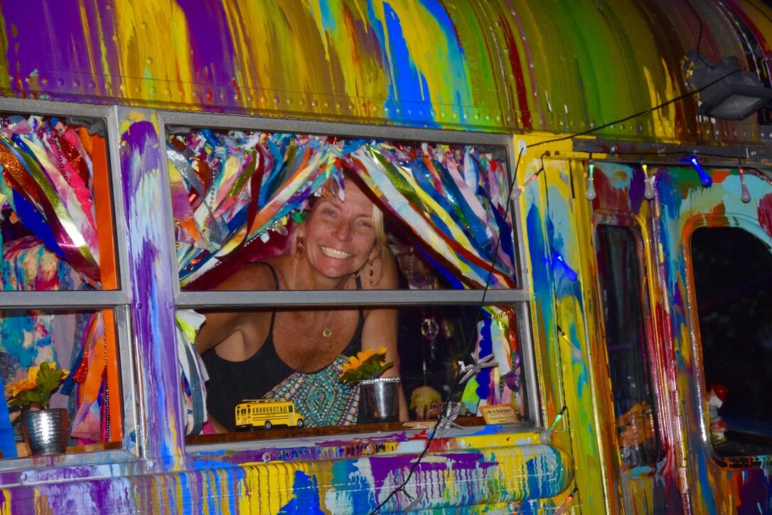 A woman leaning out SUGAREE's window at night, ribbon curtains and string lights