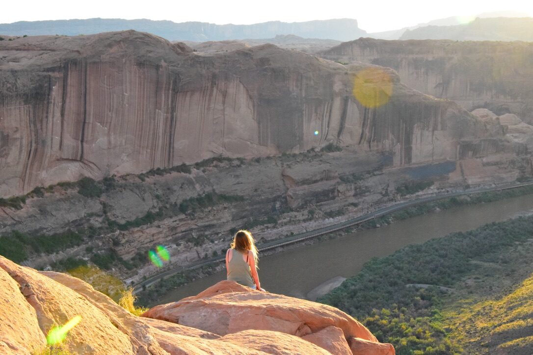 A woman sitting on a cliff edge overlooking a river canyon near Moab