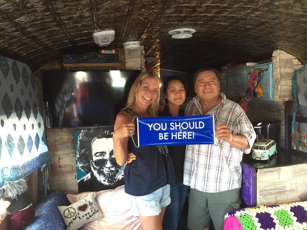 Friends inside SUGAREE holding a sign that reads 'You Should Be Here!' with a Jerry Garcia portrait on the wall